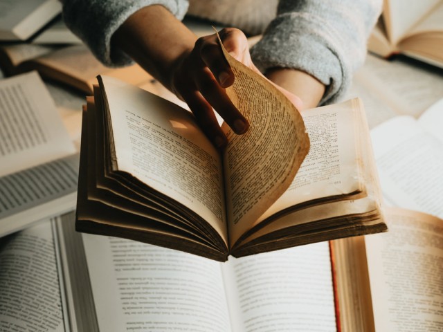 person-holds-a-book-over-a-stack-and-turns-the-page.jpg